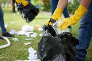 Yellow gloved hands placing trash in a black plastic bag